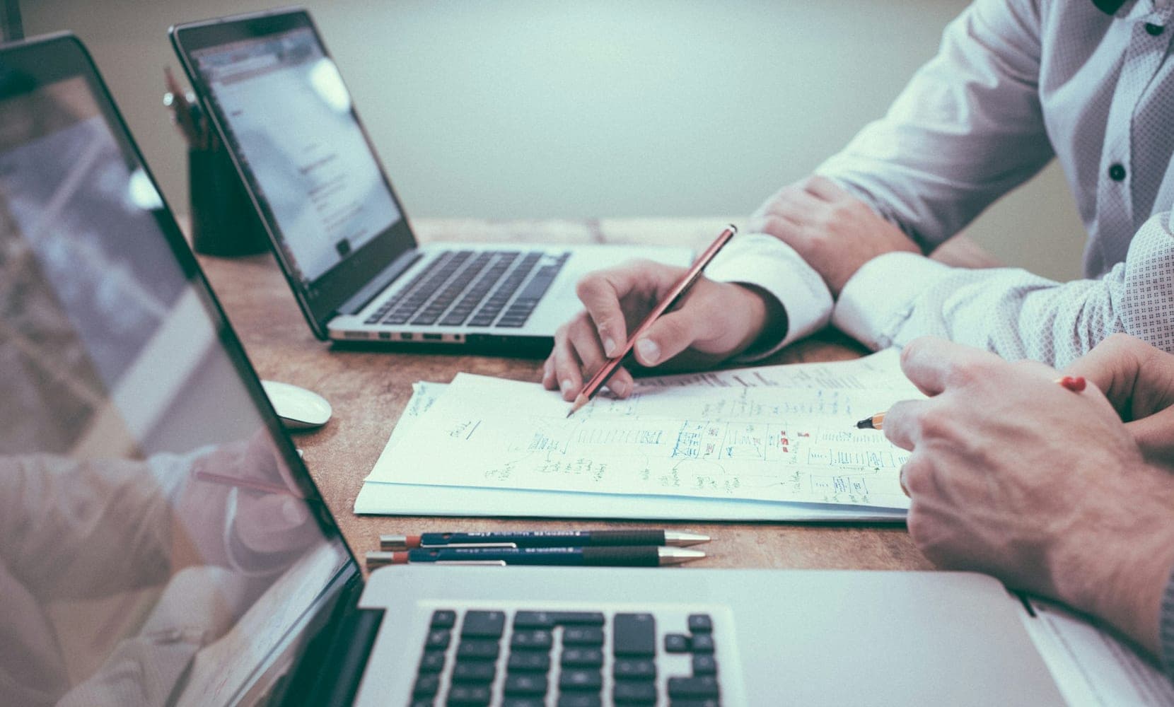 A small business owner reviews a printed monthly checklist and financial reports at a desk next to a laptop and calendar.